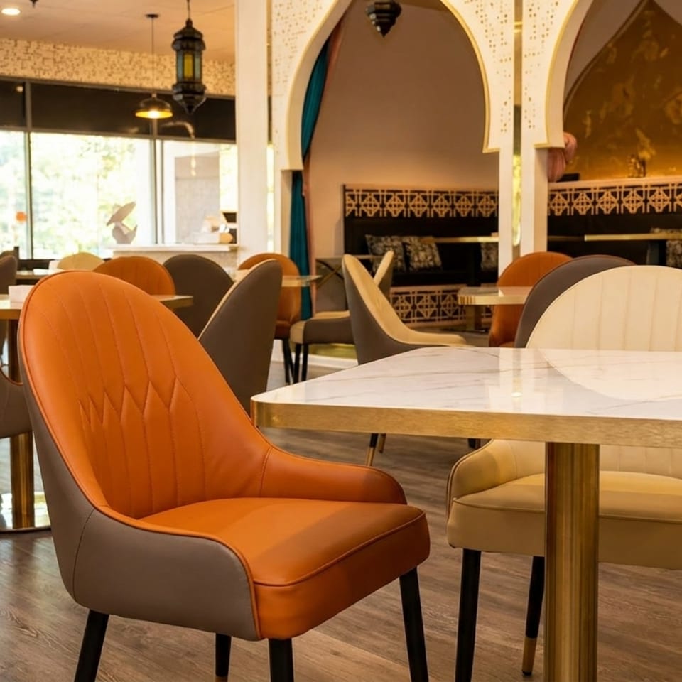 Restaurant interior with modern orange, brown, and cream chairs at marble tables, and arched alcoves.