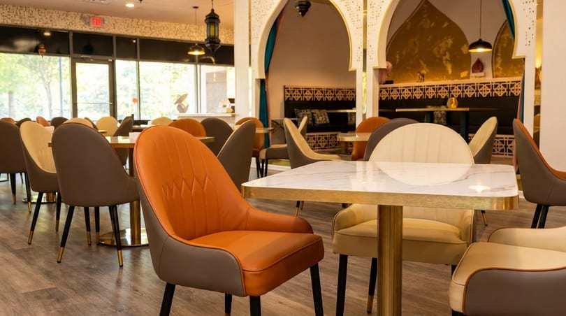A restaurant dining room with orange, brown, and cream chairs, marble tables, and Moroccan-style arches.