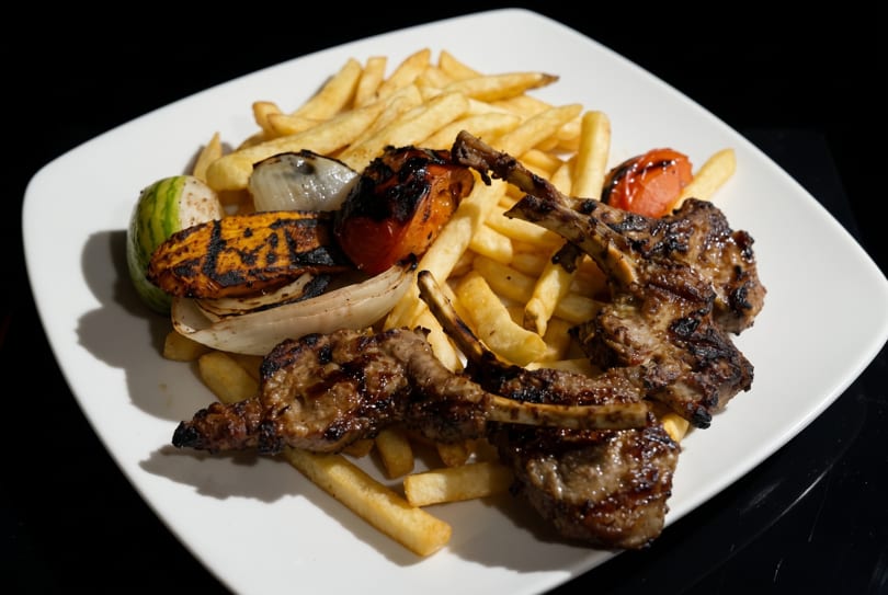 Grilled lamb chops with french fries and charred vegetables on a white plate.