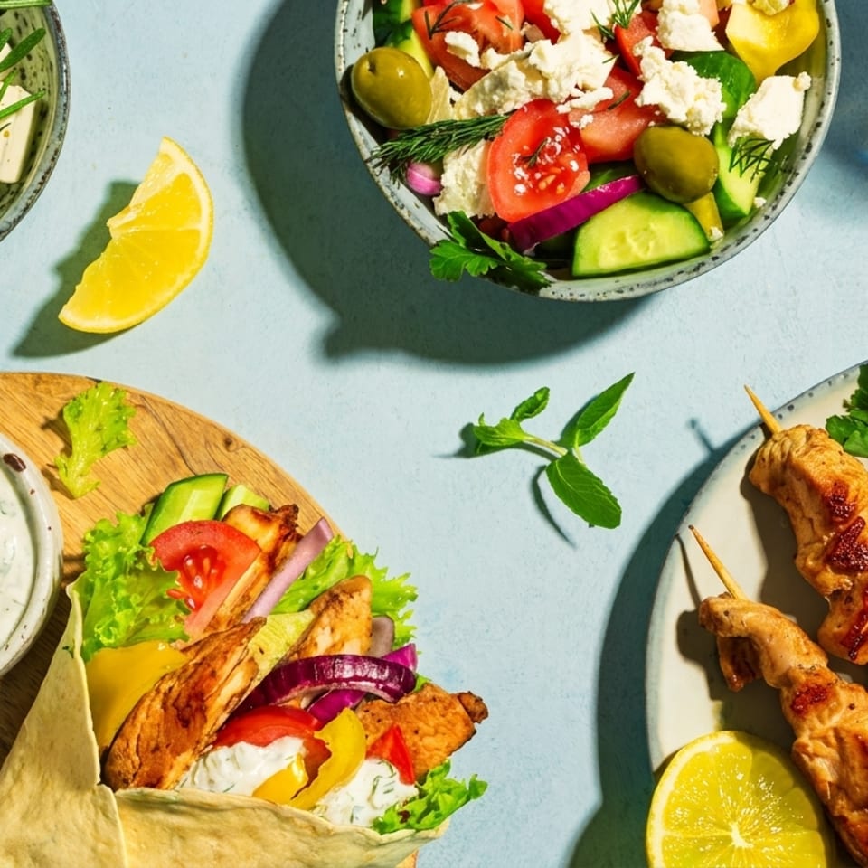 A vibrant spread of Greek dishes including chicken souvlaki, gyros, feta, olives, and salad.