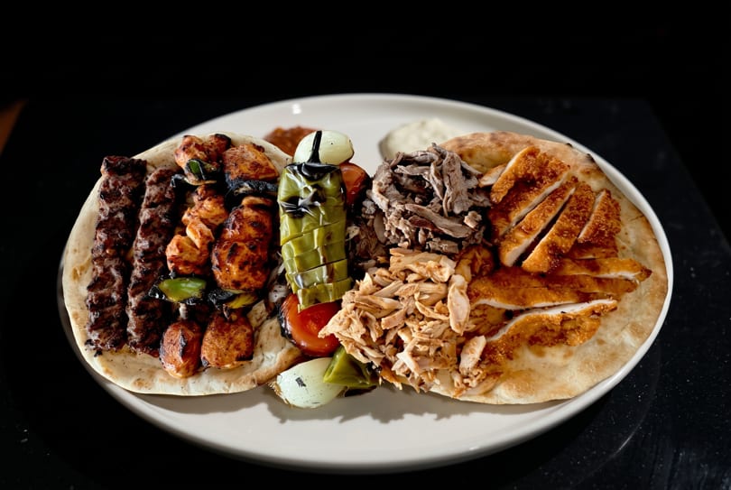 A large platter of grilled meats, including kebabs, chicken, and shawarma, served on flatbread.