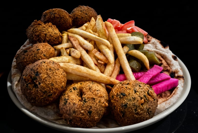 Falafel platter with fries, tomatoes, pickles, and pink pickled turnips on pita bread.